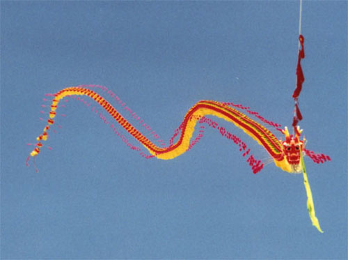 A long Chinese dragon kite with red and yellow segments flying against a blue sky