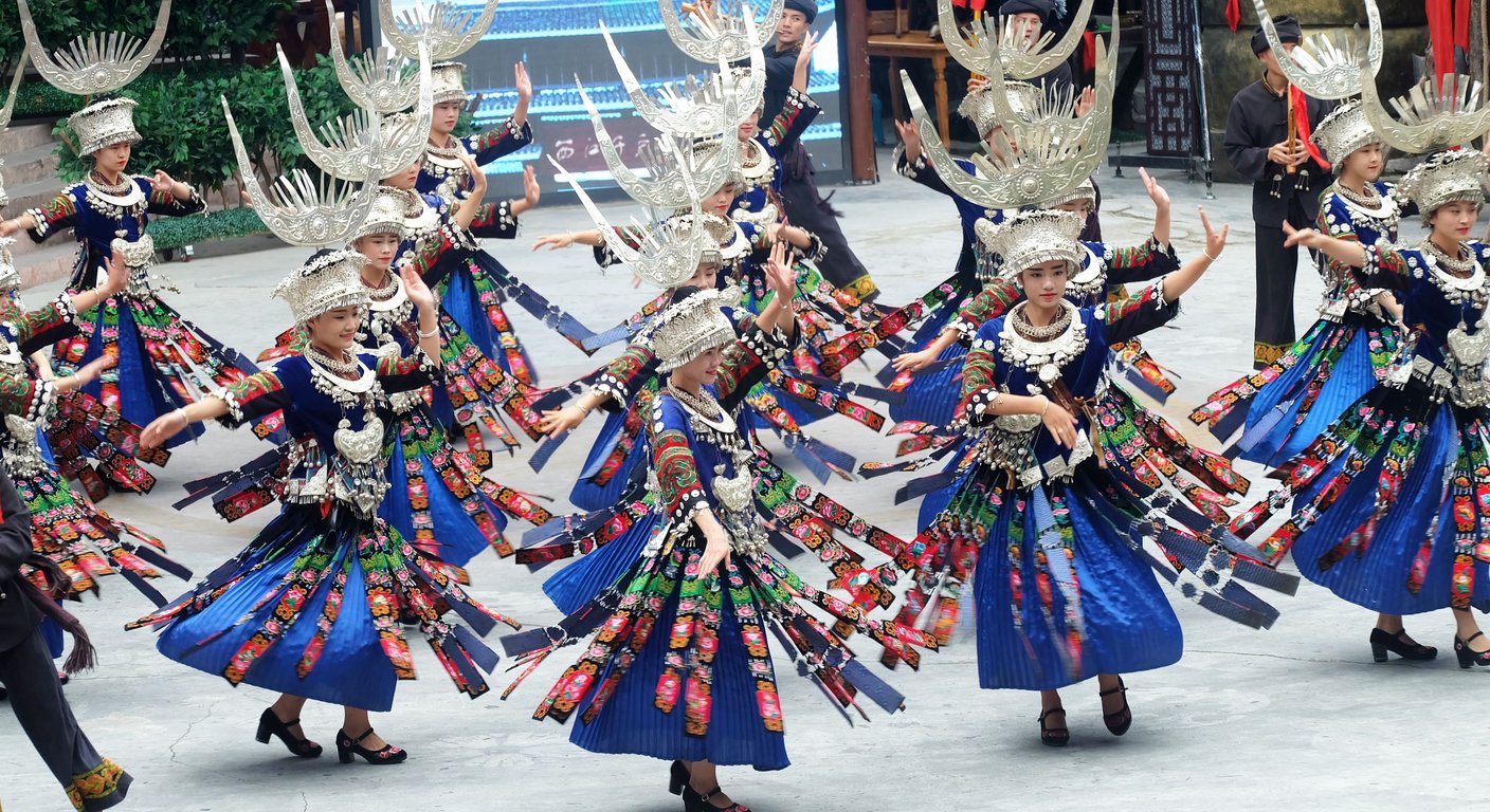 Miao women dancing in festival dress with silver horned headdresses and indigo-blue pleated skirts