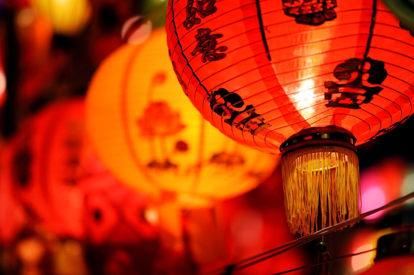 Close-up of a glowing red Chinese lantern painted with calligraphy, more red lanterns blurred behind it