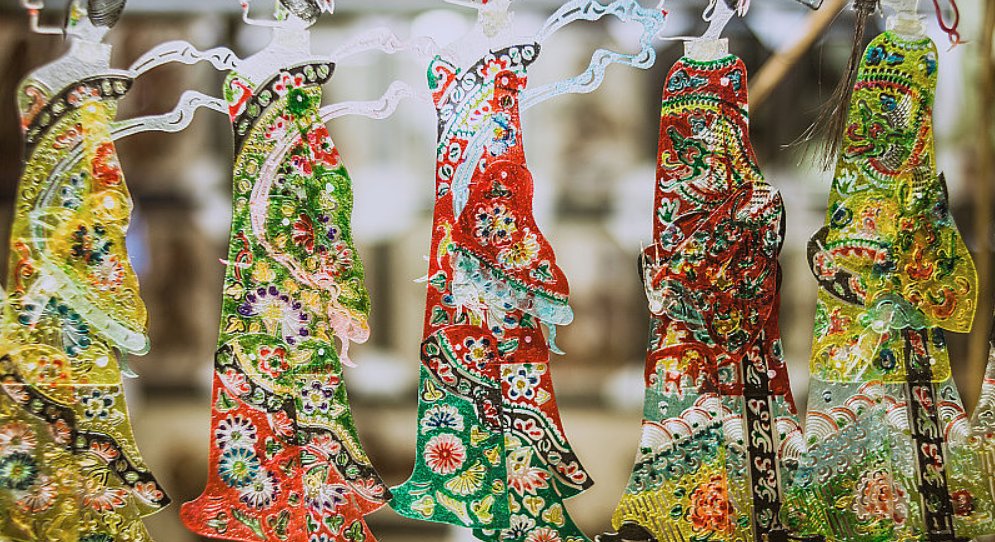 A row of colorful translucent shadow puppets hanging, each carved and painted by hand