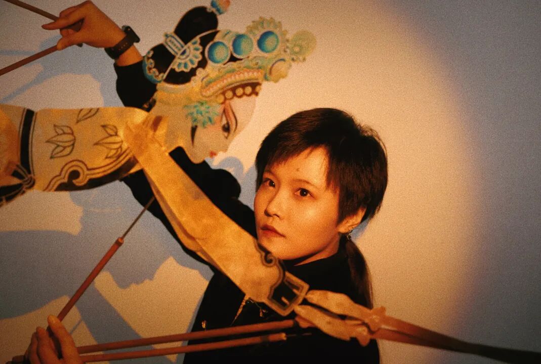 Sun Bingqing manipulating a leather puppet with rods behind the screen