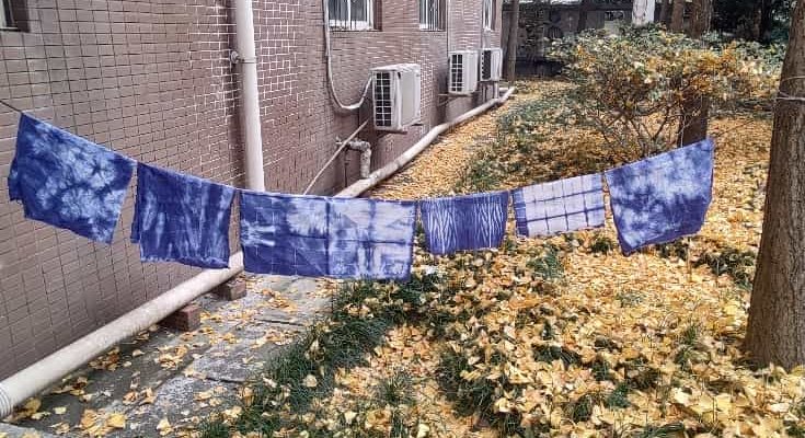Freshly dyed blue-and-white tie-dye cloths drying on a line outdoors