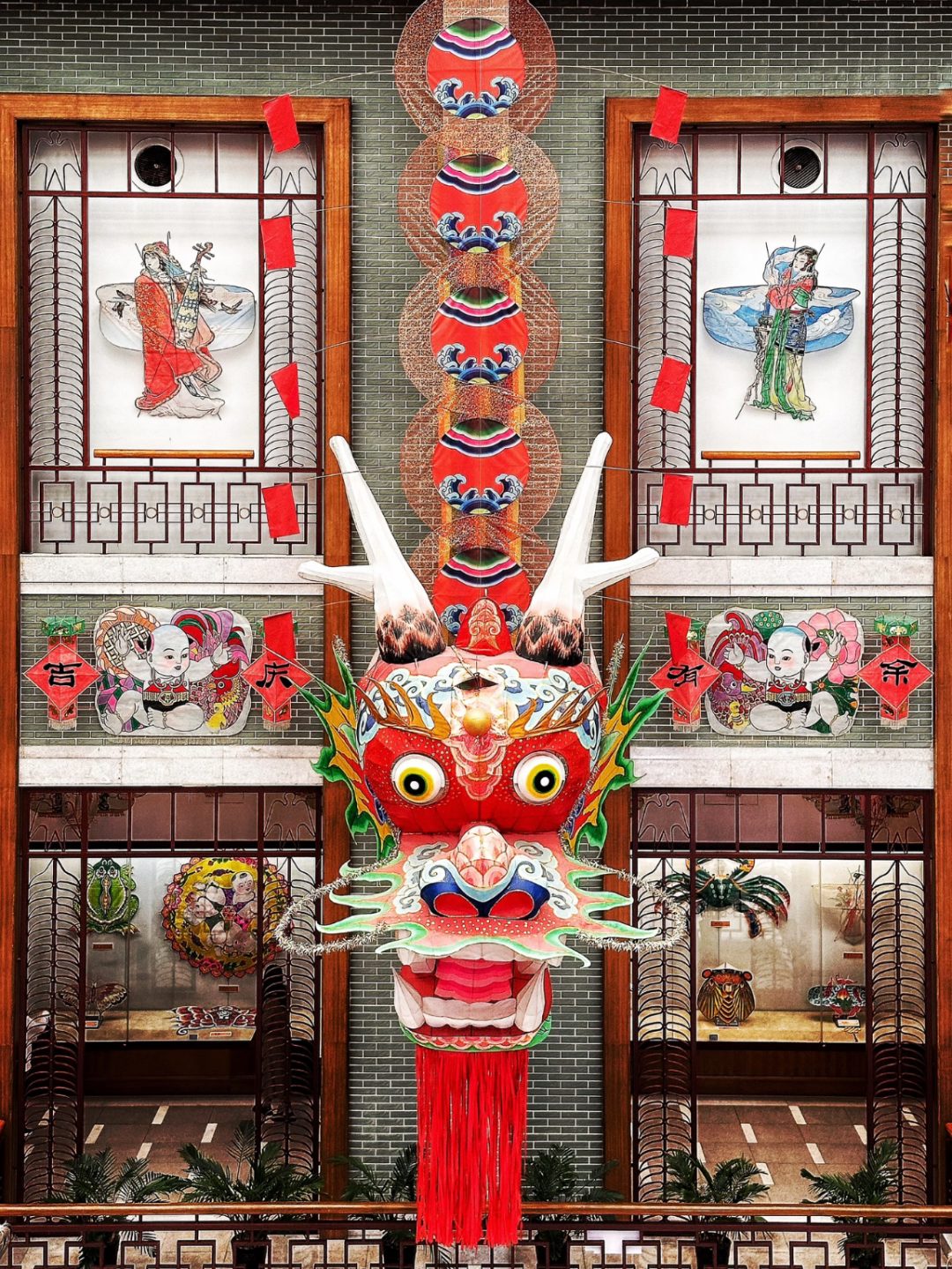 A giant Weifang dragon-head centipede kite hanging in a traditional Chinese hall, woodblock new-year prints on the walls