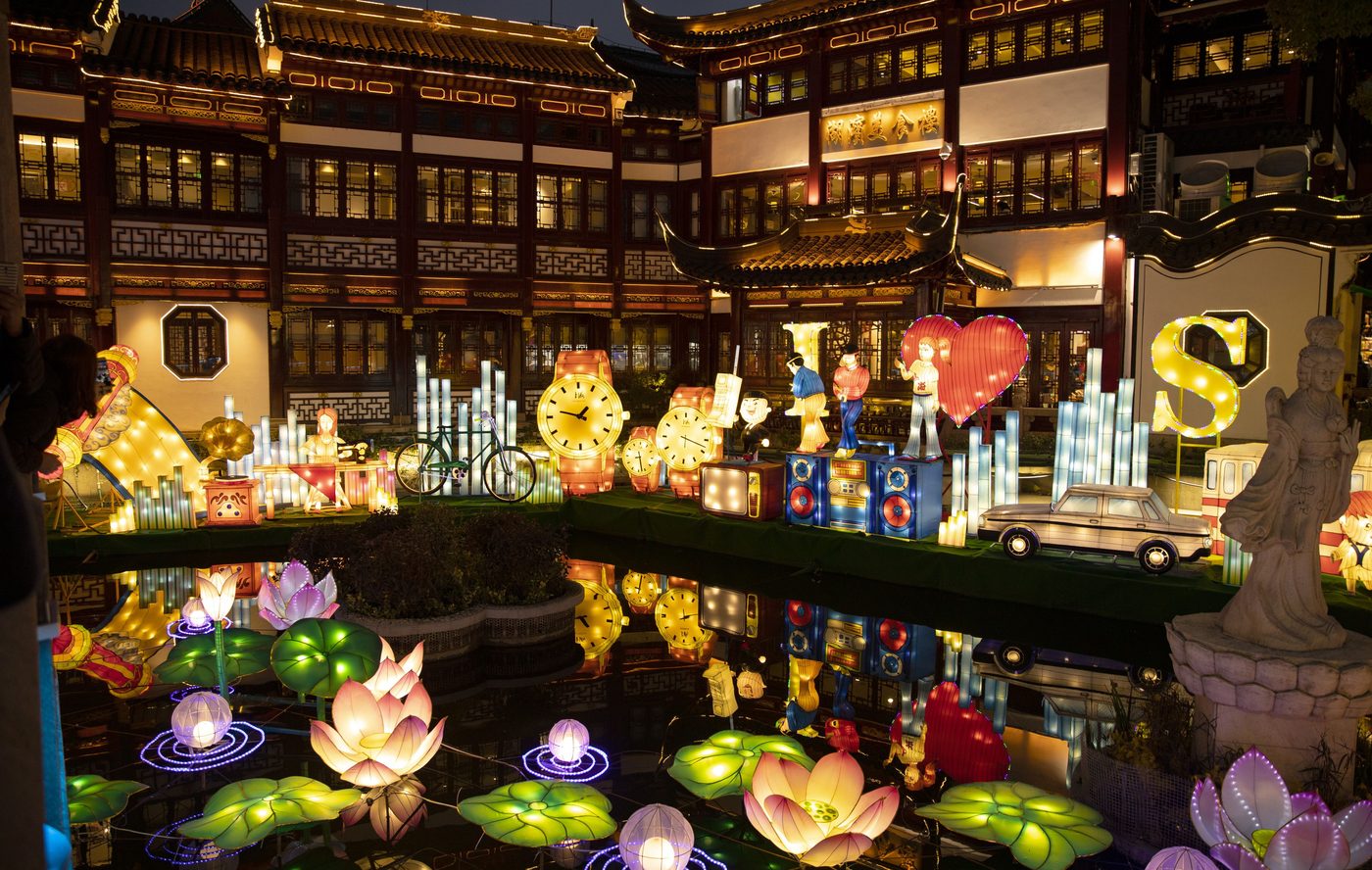 A modern Chinese lantern fair at night: illuminated lotus lanterns floating on water in front of traditional pavilion architecture
