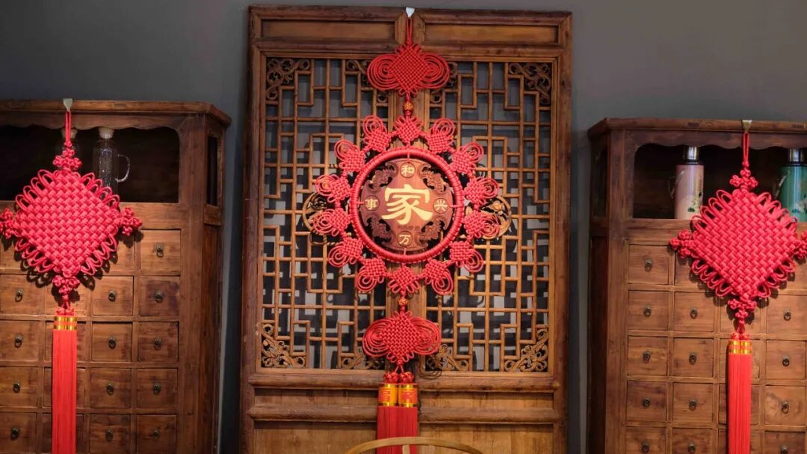 A round 'family' character knot medallion hanging on a traditional wooden lattice window, large pan chang knots on cabinets to both sides