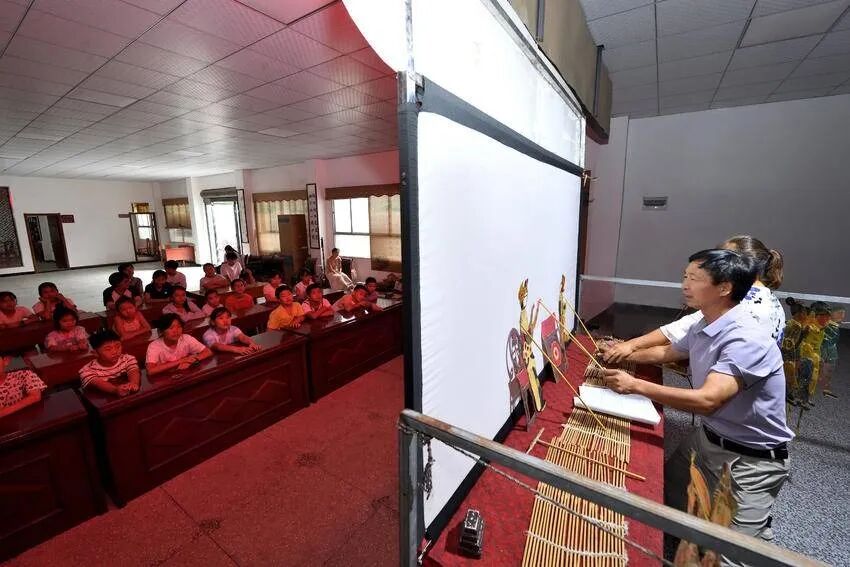 Children in a summer care class watching Zou Guichang perform behind the screen
